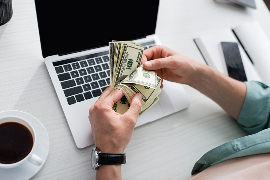 close-up of a man holding dollar banknotes while sitting in front of his laptop, illustrating the financial rewards of 'making money with wordpress affiliate'