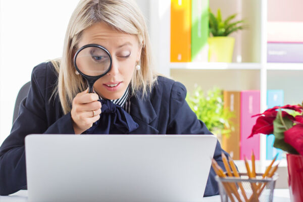 Woman looking through a magnifying glass into the computer concept image for the importance for checking compatibility